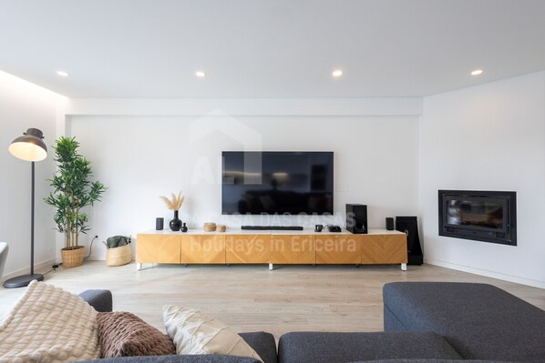 A modern living room with a flat-screen TV, wooden entertainment unit, and a fireplace. - Terence Apartment by Acasadascasas (Mafra)