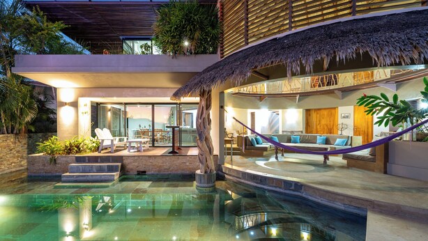 Een modern resort met een zwembad, terras en een loungegedeelte met rieten dak.