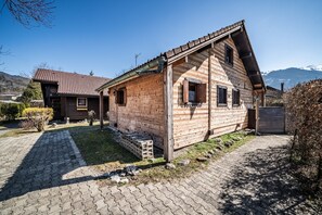 Una casa de madera con techo inclinado, camino de entrada pavimentado y montañas al fondo.