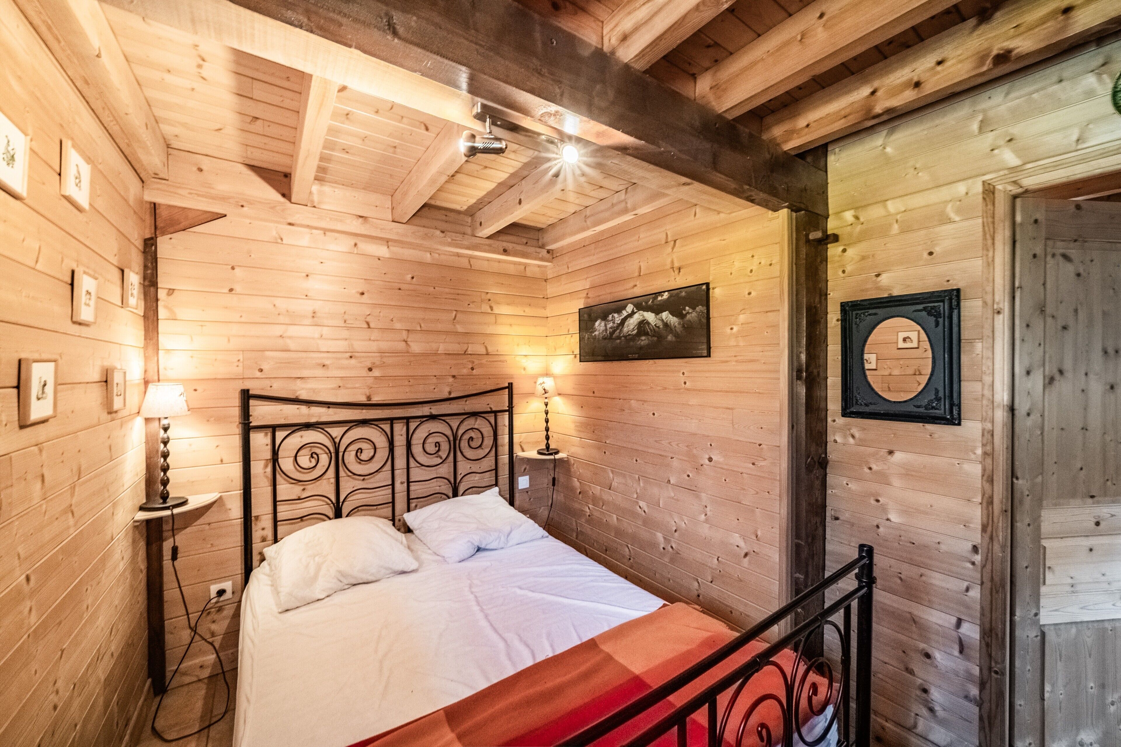 Camera da letto con rivestimenti in legno, un letto, due lampade da comodino, un quadro appeso alla parete e una porta con uno specchio.
