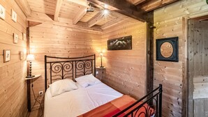 A wooden-paneled bedroom with a bed, two bedside lamps, a framed picture on the wall, and a door with a mirror. - Chalet “8p Comfort – Le Gaby” with Mountain View and Wi-Fi (Verchaix)