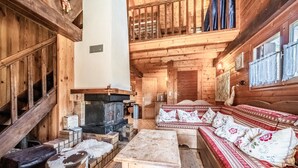 A log cabin interior with a fireplace, wooden furniture, and a staircase. - Chalet “8p Comfort – Le Gaby” with Mountain View and Wi-Fi (Verchaix)