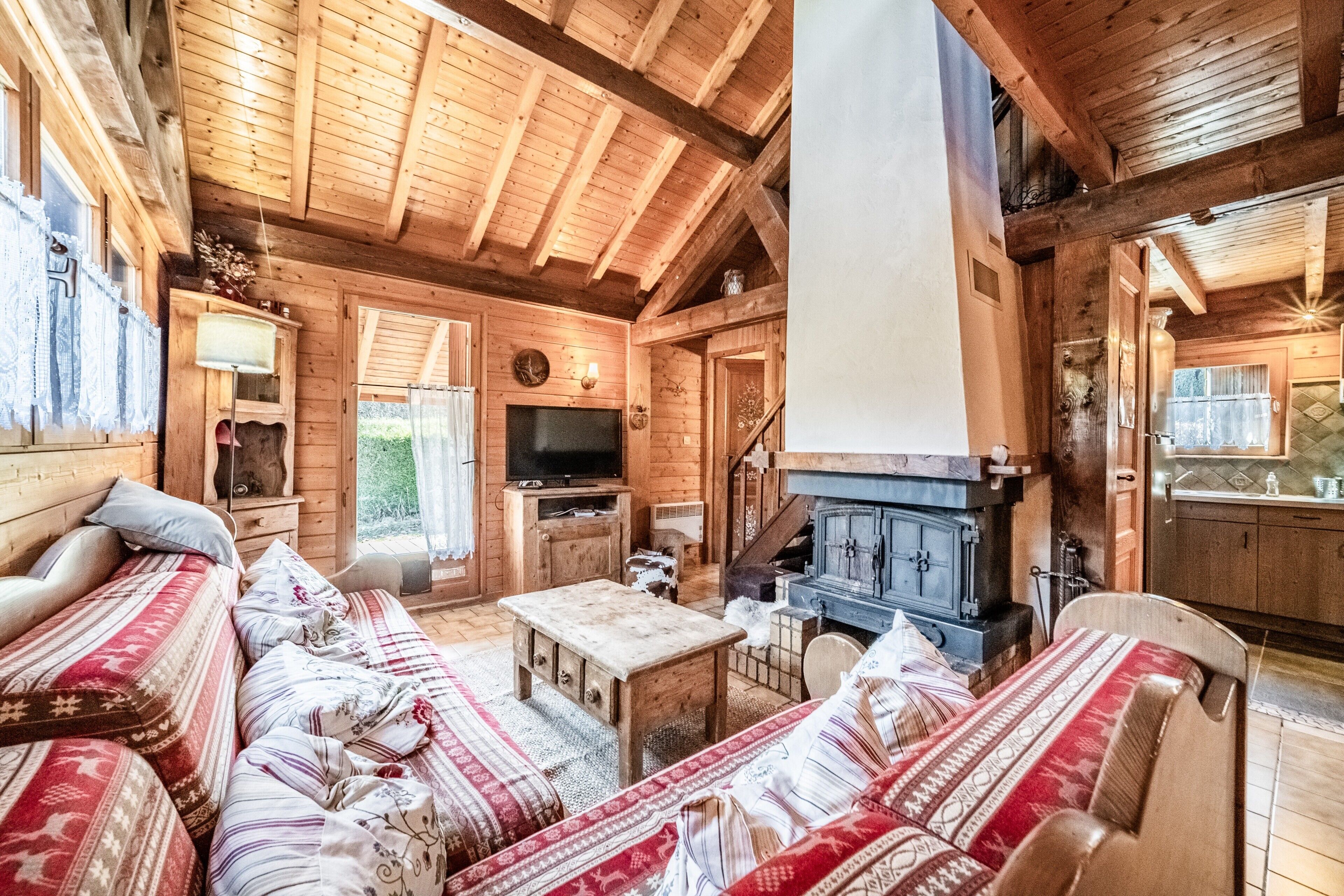 Interno di una baita in legno con divano, televisione, camino e travi a vista.