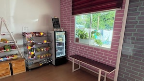 A room with a brick wall, a window with a view of greenery, a bench, a refrigerator stocked with snacks, and shelves with packaged goods. - OYO 91278 5minutes Lodge (Kota Kinabalu)