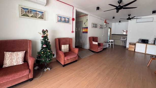 A spacious living room with a wooden floor, red armchairs, a decorated Christmas tree, and a kitchen area with a microwave and sink. - OYO 91278 5minutes Lodge (Kota Kinabalu)