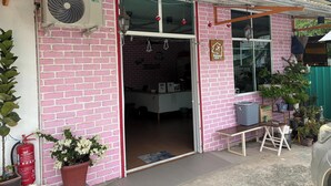 A pink brick building with a sliding glass door entrance, a fire extinguisher, a potted plant, and a bench outside. - OYO 91278 5minutes Lodge (Kota Kinabalu)