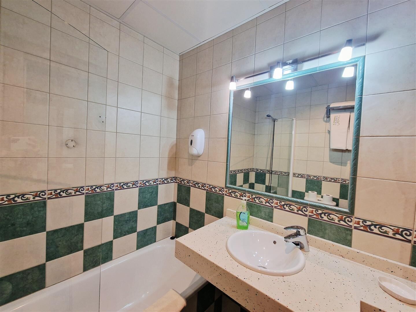 Un baño con bañera, lavamanos, espejo y dispensador de jabón.
