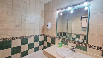 Un baño con bañera, lavamanos, espejo y dispensador de jabón.