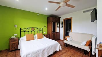 Een slaapkamer met een bed, nachtkastje, bank, plafondventilator en televisie.