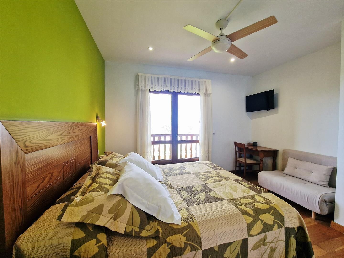 Un dormitorio con cama, una silla, televisión y balcón.