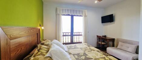 Un dormitorio con cama, una silla, televisión y balcón.