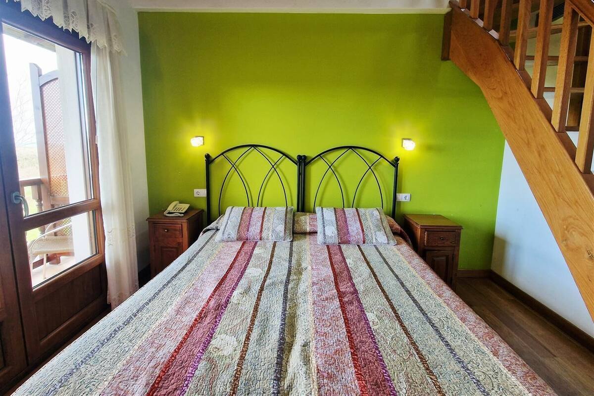 A bedroom with a green wall, a bed with a striped bedspread, two bedside lamps, and a wooden staircase.