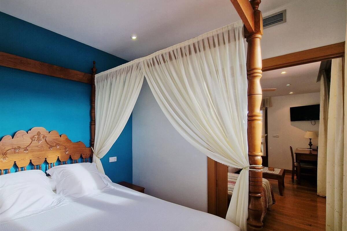 A bedroom with a four-poster bed, a blue accent wall, and a wooden floor.