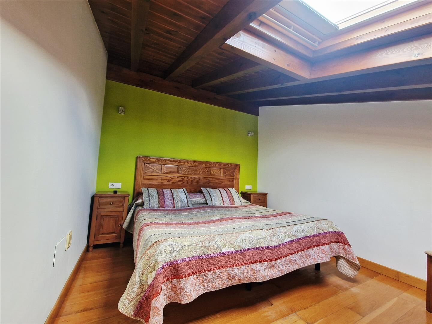 A bedroom with a wooden bed, green walls, and a skylight.