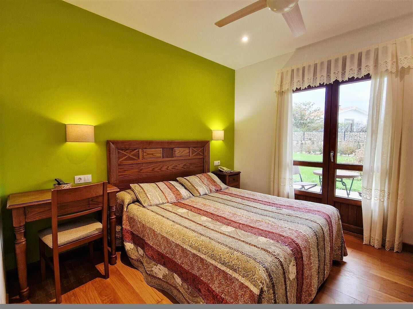 Una camera da letto con un letto in legno, due lampade sui comodini, una scrivania e vista all'esterno tramite una porta in vetro.