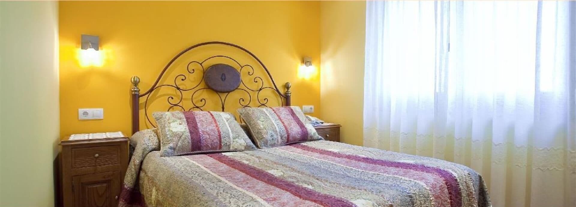 A bed with a patterned bedspread, a headboard with a circular design, and two wall-mounted light fixtures.