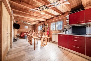 A wooden interior with a dining area, red kitchen cabinets, and a mounted television. - Chalet “8p - L’œillet des Glaciers” with Mountain View and Wi-Fi (Verchaix)