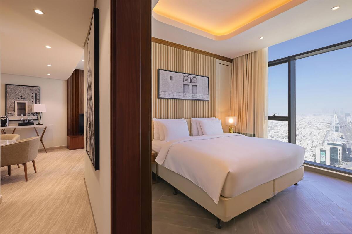 A modern hotel room with a large bed, a desk, and a view of the city.