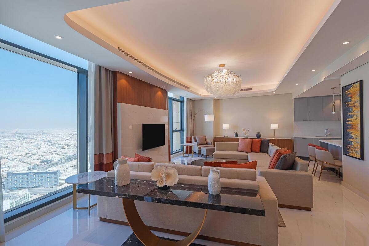 A modern living room with a glass coffee table, a sofa set, a television, and a dining area.