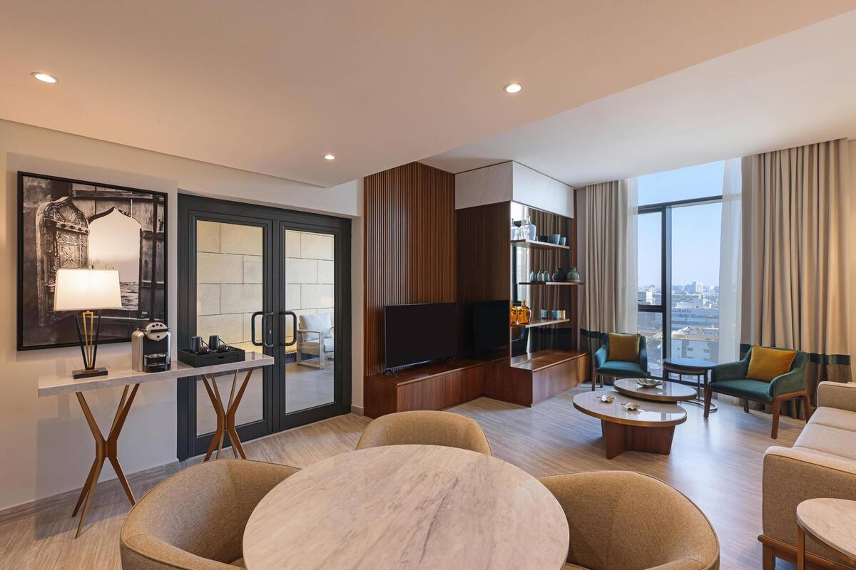 A modern hotel room with a large TV, seating area, and a city view.