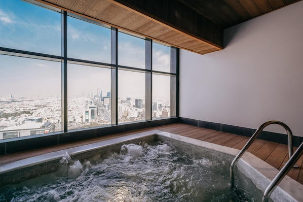 A hot tub with a city view, large windows, and wooden flooring.