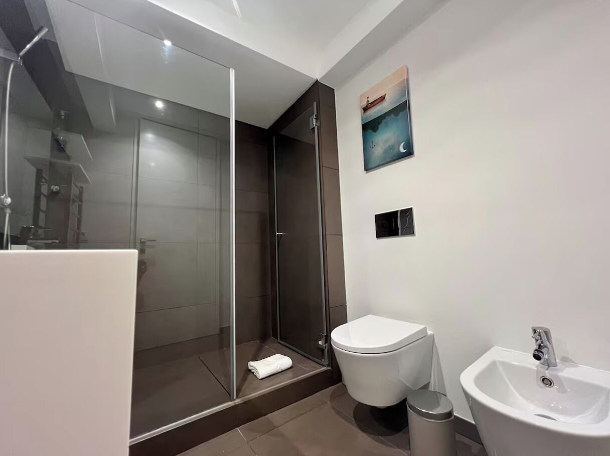 A modern bathroom with a glass-enclosed shower, a white toilet, and a sink.
