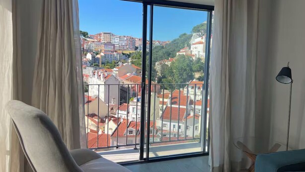 Habitació amb una gran porta corredissa de vidre que dona a un balcó, una cadira, una làmpada i un sofà.