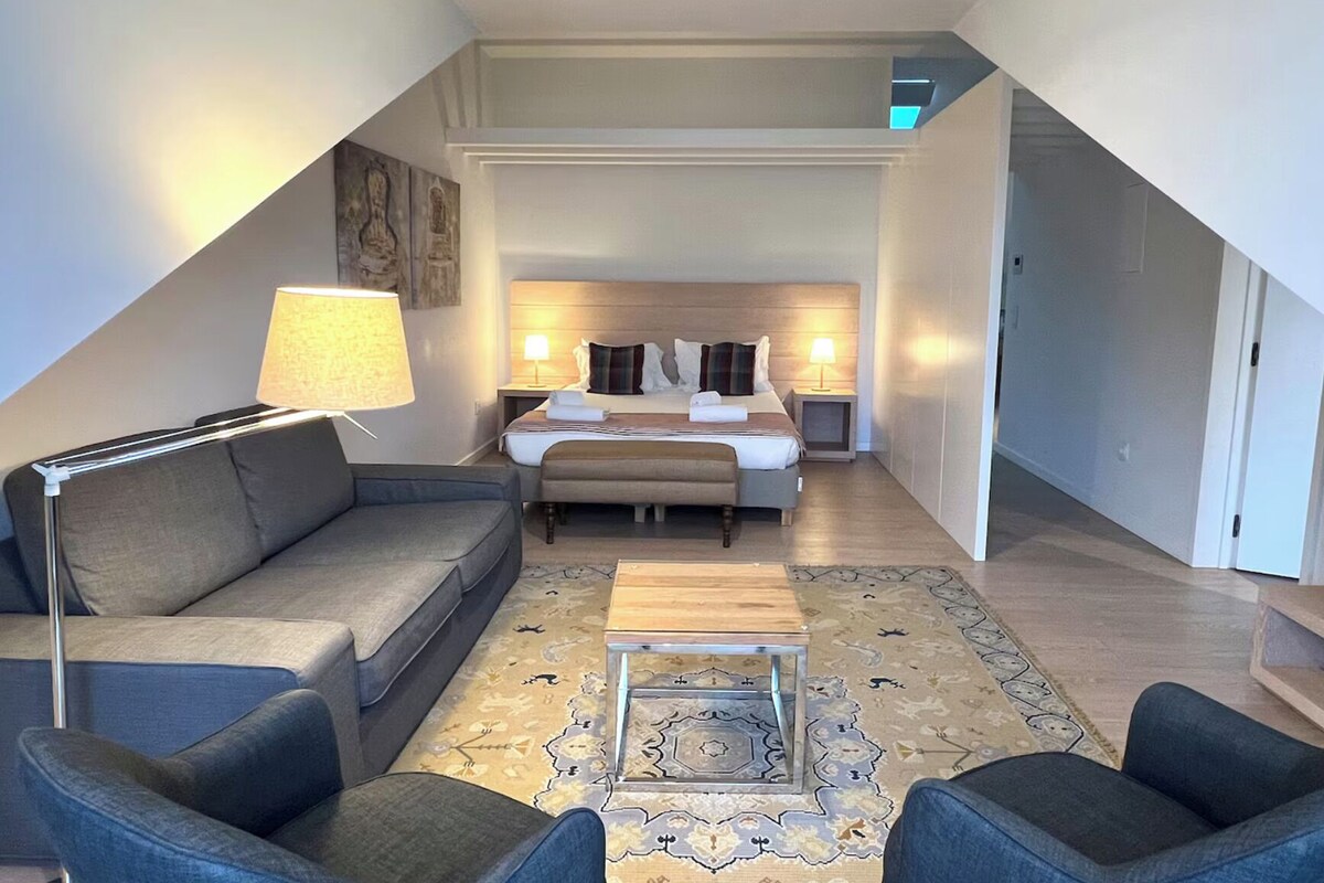 Habitació d'hotel moderna amb llit, sofà, taula de cafè i làmpada.