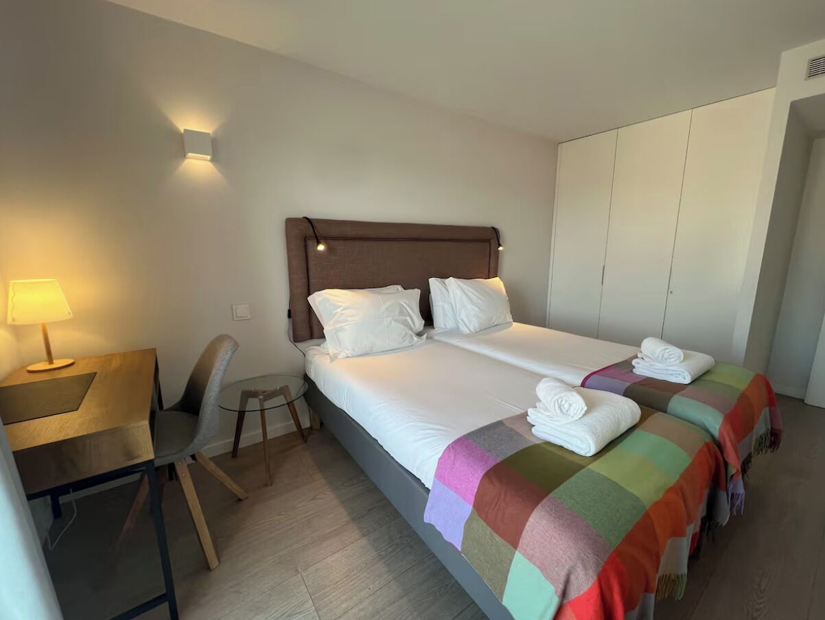 A hotel room with a bed, a desk, a chair, and a wardrobe.