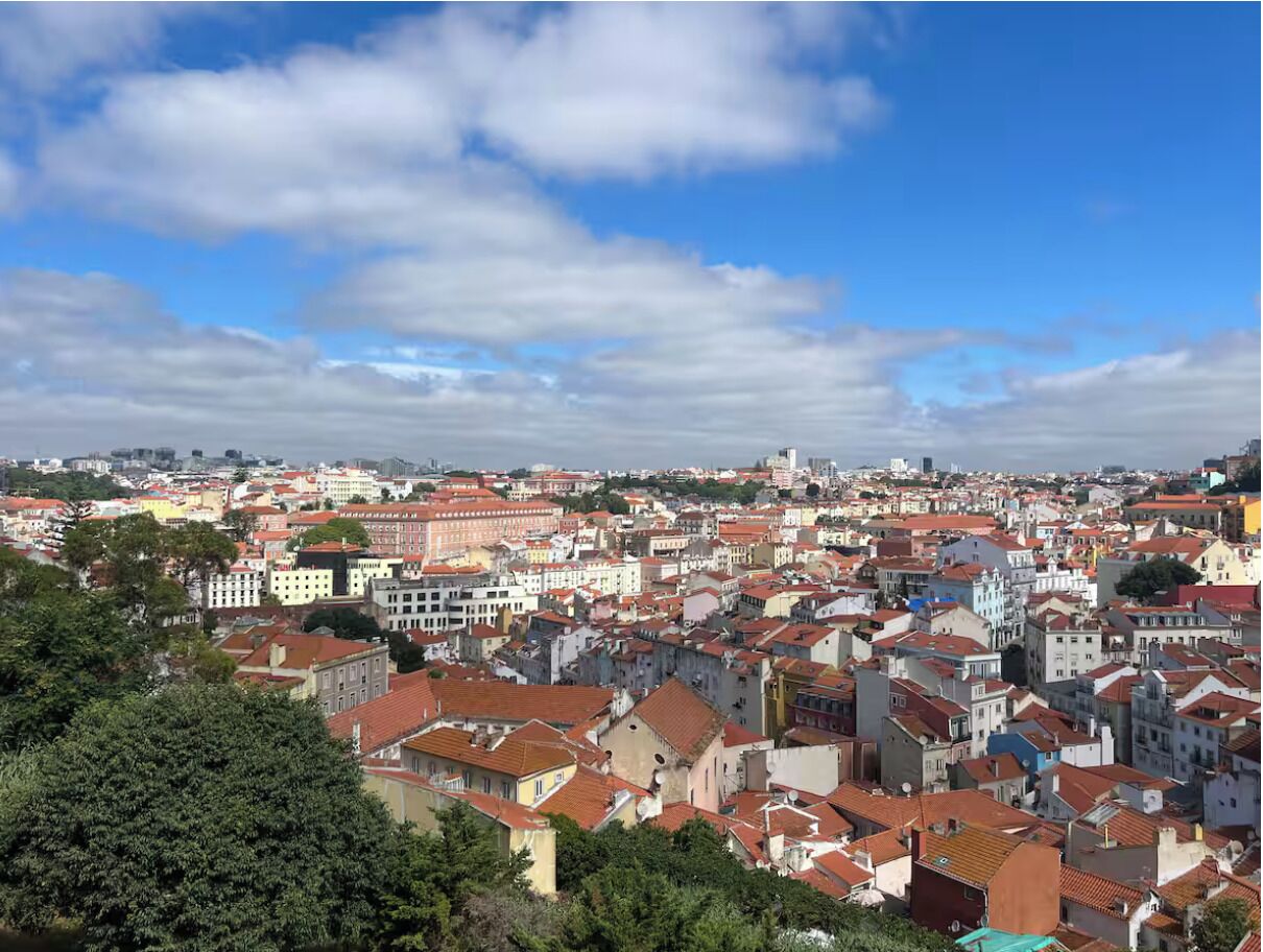 A densely packed urban area with red-tiled roofs and a mix of building styles, under a partly cloudy sky.
