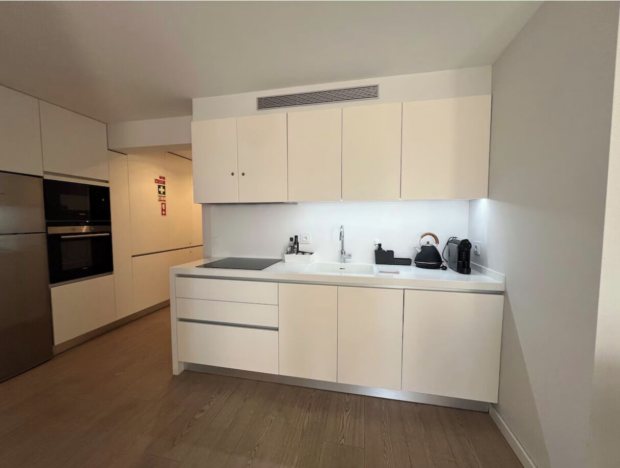 A modern kitchen with white cabinets, a built-in oven, a sink, and a kettle.