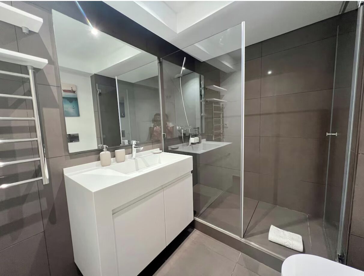 A modern bathroom with a glass-enclosed shower, a white vanity with two sinks, and a large mirror.