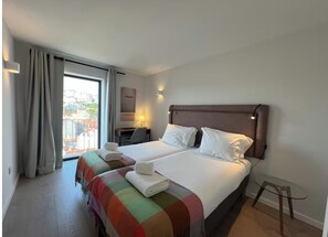 A hotel room with two beds, a desk, and a view of buildings through a large window. - Amazing View in Castle View (Lisbon)