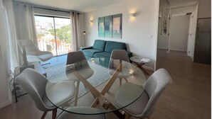 Un saló modern amb una taula de dinar de vidre, quatre cadires, un sofà color turquesa i una finestra gran amb cortines.