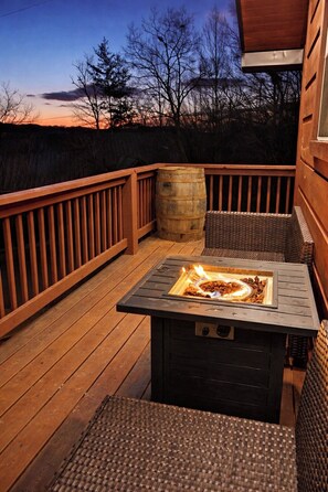 An outdoor deck with a fire pit table, wooden railings, wicker furniture, and a barrel. - Moonshine Still Cabin · Hot Tub, Fire Pit & Views (Sevierville)