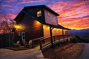 A wooden cabin with a porch, a fireplace, and a scenic mountain backdrop. - Historic Moonshine Still Cabin, Hot Tub & Fire Pit (Sevierville)