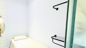 A small, modern room with a single bed, a glass partition, and a wall-mounted shelf. - Tortuga Suite: comfortable and functional, close to the beach. (Guarujá)