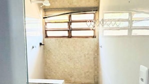 A small, compact bathroom with a toilet, a shower area, and a window providing natural light. - Tortuga Suite: comfortable and functional, close to the beach. (Guarujá)