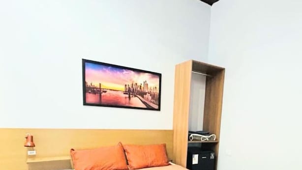 A bedroom with a bed, a nightstand, a picture of a cityscape, and a wardrobe. - Tortuga Suite: comfortable and functional, close to the beach. (Guarujá)