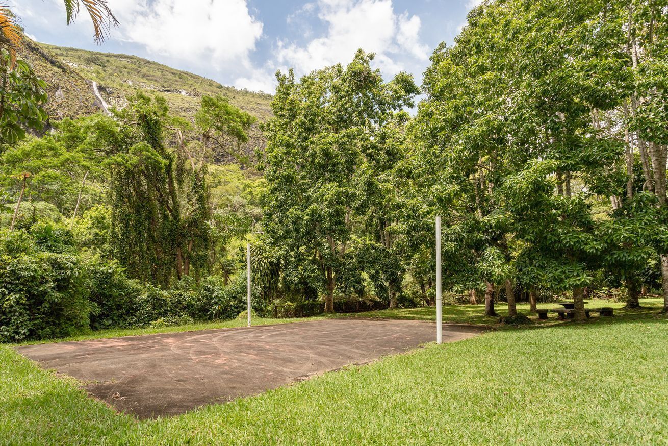 A paved area surrounded by lush greenery and trees, with a hill in the background.