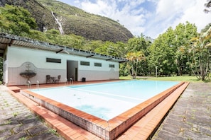 A swimming pool with a tiled deck, a covered seating area, and a mountain backdrop. - S tio com Piscina e Lareira a 10 min de Itaipava (Petrópolis)