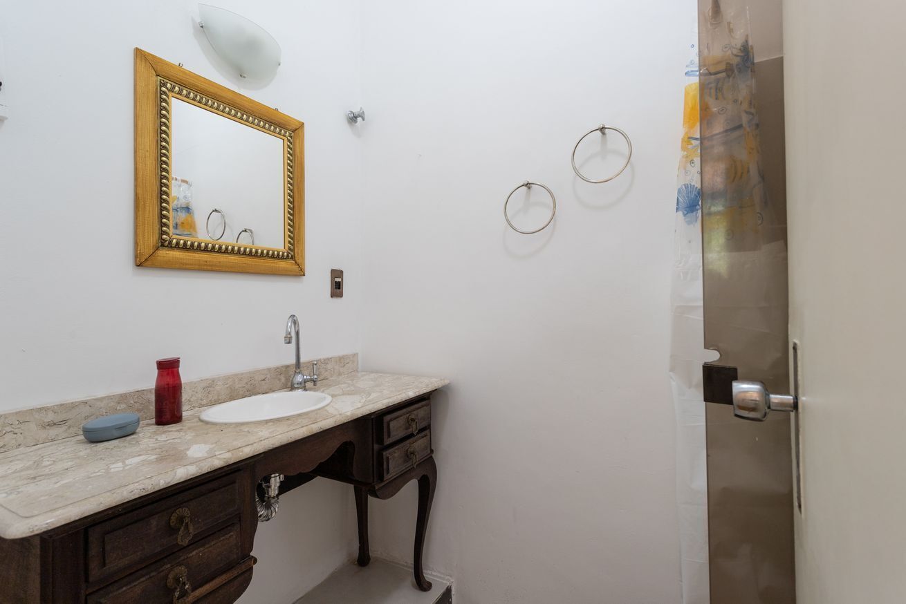 A bathroom with a marble sink, wooden vanity, a gold-framed mirror, and a shower door.