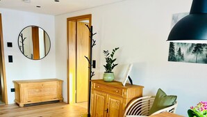 A room with a wooden dining table, a woven rug, a mirror, a cabinet, and a hanging pendant light.