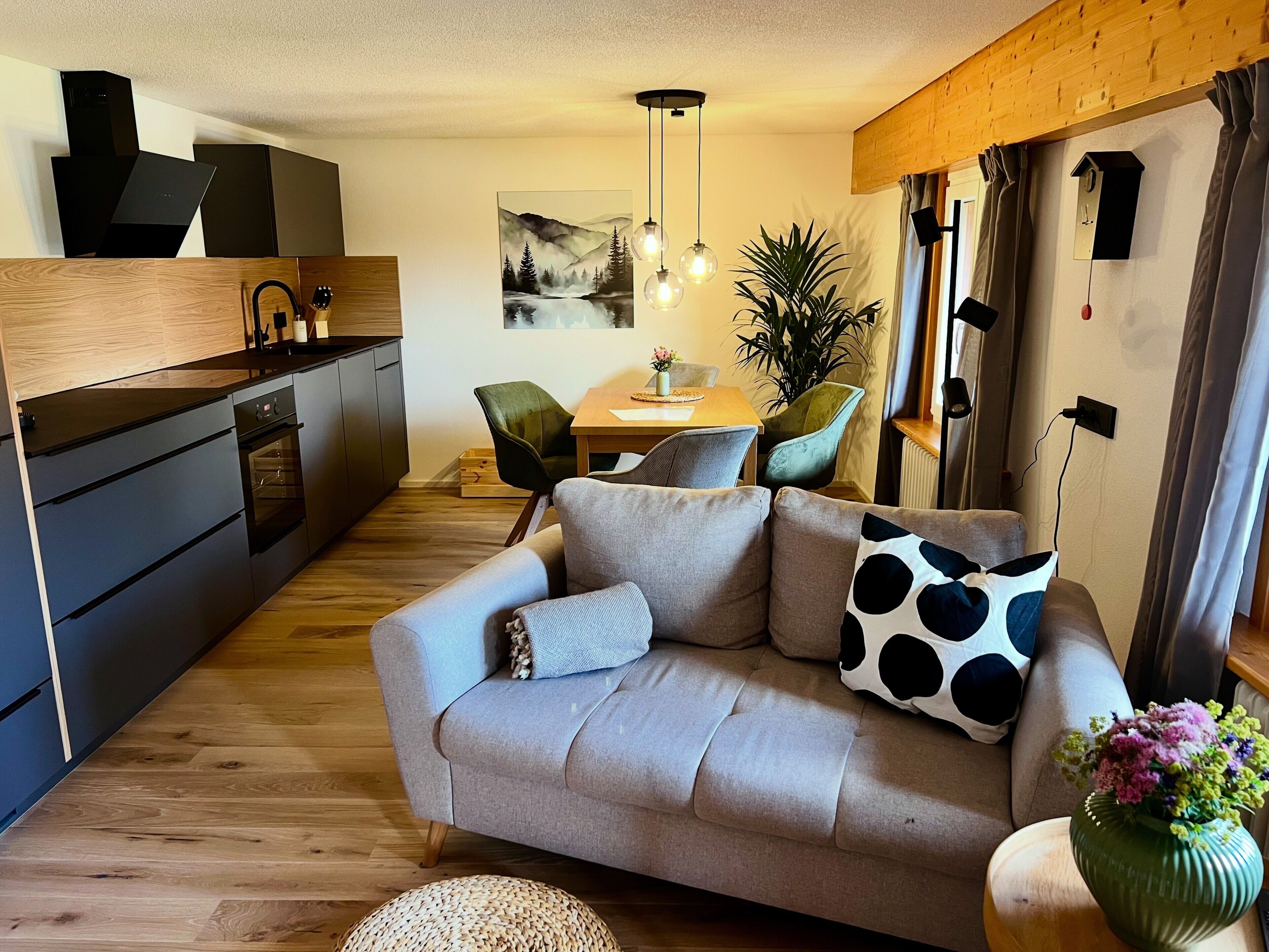 A modern living space with a sofa, dining table, chairs, and a kitchen area.