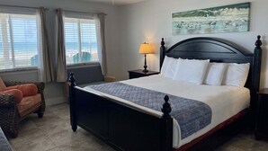 A hotel room with a large bed, a ceiling fan, a painting of birds, a window with curtains, and a chair. - Beachgate Condo Suites And Hotel 237+239 2 Bedroom Condo (Port Aransas)