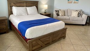 A bedroom with a wooden bed, a beige sofa, and a nightstand with a lamp. - Beachgate Condo Suites And Hotel 536+537b 2 Bedroom Condo (Port Aransas)