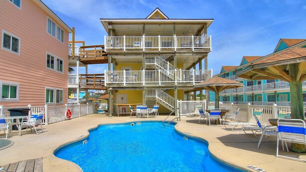 A multi-story hotel with a swimming pool, outdoor seating, and a lifeguard stand. - Beachgate Condo Suites And Hotel 536+537b 2 Bedroom Condo (Port Aransas)