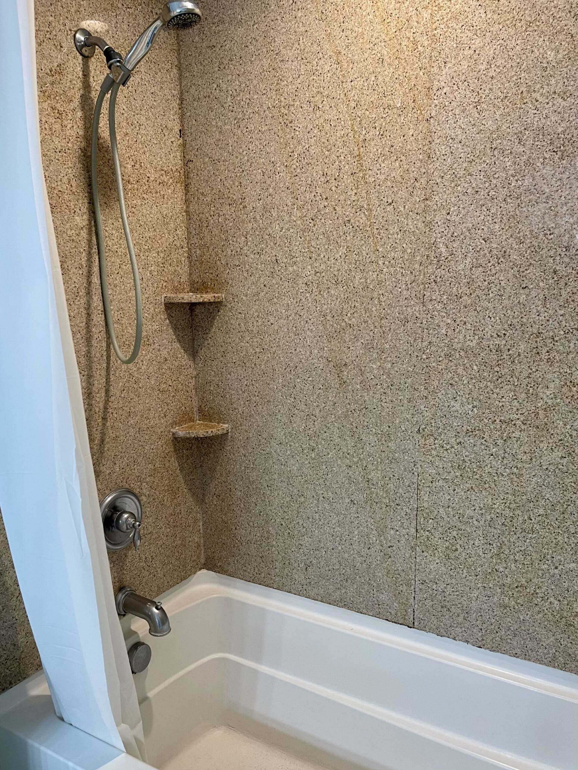 A corner of a bathroom with a bathtub, a shower head, and a towel rack.