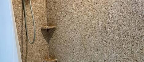 A corner of a bathroom with a bathtub, a shower head, and a towel rack.