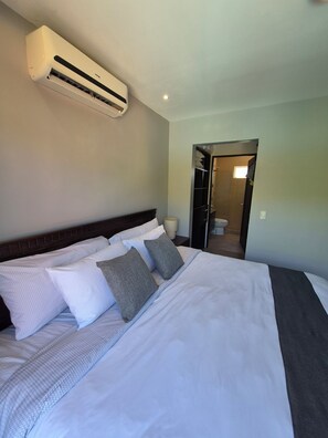 A hotel room with a large bed, a wall-mounted air conditioner, and a bathroom visible through an open door. - Beautiful home in gated community on private beach and Golf course in Costa Rica (Tambor)